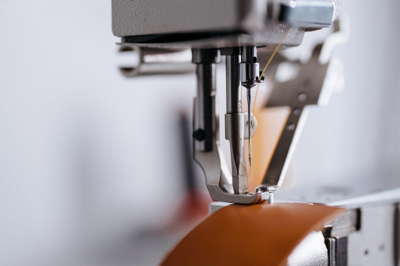 Detailed shot of a sewing machine's needle and presser foot working on leather material.